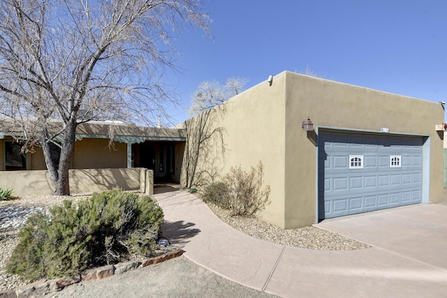 pueblo-style home with stucco siding, concrete driveway, and a garage