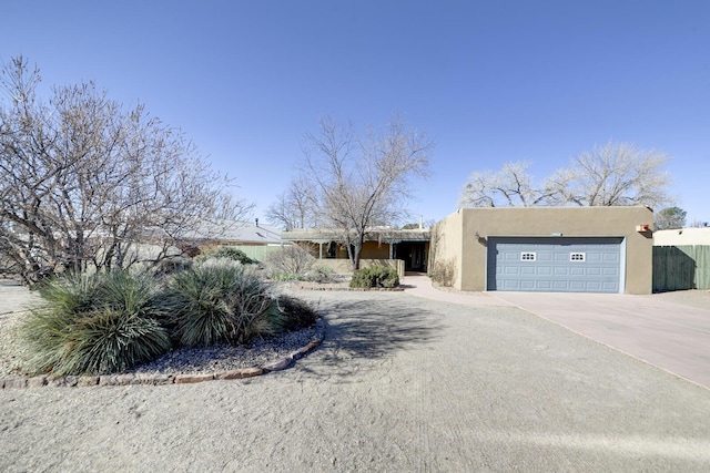 southwest-style home with concrete driveway, fence, a garage, and stucco siding