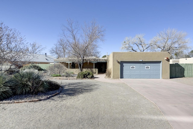 southwest-style home featuring fence, a garage, driveway, and stucco siding