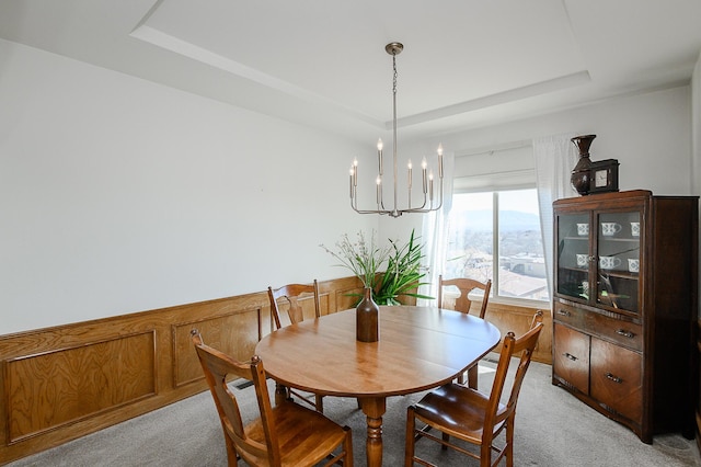 dining space with a raised ceiling, wainscoting, a chandelier, and light carpet