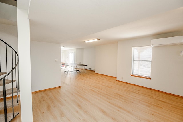 spare room featuring light wood finished floors, a baseboard heating unit, baseboards, stairs, and a wall mounted AC