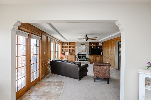 living area with built in features, light colored carpet, french doors, a fireplace, and a ceiling fan