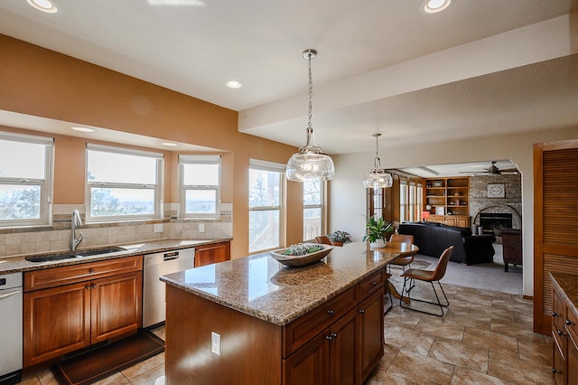 kitchen with a kitchen island, open floor plan, light stone counters, stainless steel dishwasher, and a sink