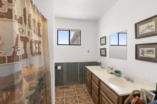 full bath with double vanity, stone finish floor, a wainscoted wall, and a sink