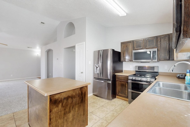 kitchen featuring a center island, light tile patterned floors, appliances with stainless steel finishes, arched walkways, and a sink