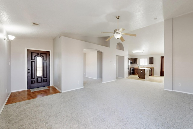 unfurnished living room featuring a ceiling fan, arched walkways, a wealth of natural light, and light carpet