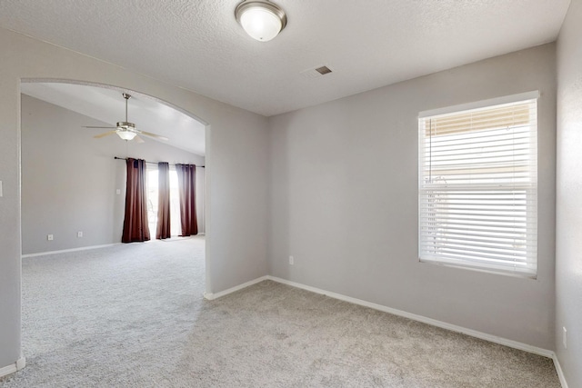 spare room with carpet, vaulted ceiling, arched walkways, a textured ceiling, and a ceiling fan