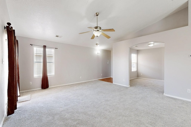 carpeted empty room featuring vaulted ceiling, plenty of natural light, a ceiling fan, and arched walkways