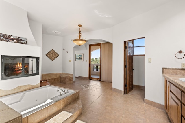 bathroom with a glass covered fireplace, a wealth of natural light, vanity, and a tub with jets