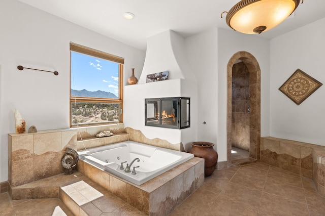 bathroom with a jetted tub, a multi sided fireplace, and tiled shower