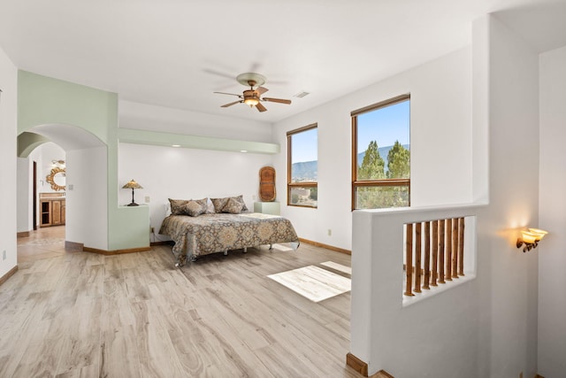 bedroom featuring light wood finished floors, arched walkways, baseboards, visible vents, and ceiling fan