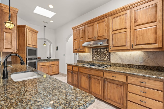 kitchen featuring stainless steel appliances, arched walkways, a sink, a skylight, and under cabinet range hood