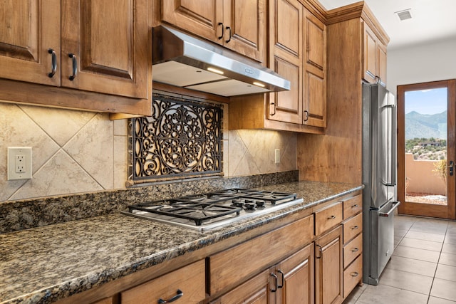 kitchen featuring brown cabinetry, decorative backsplash, under cabinet range hood, and stainless steel appliances