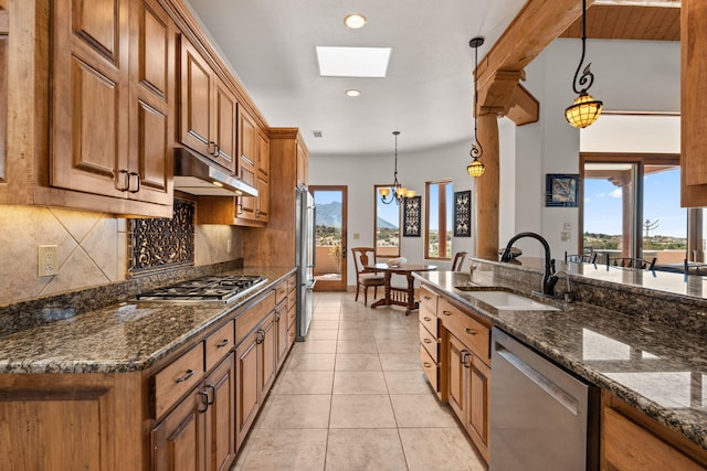 kitchen with brown cabinetry, under cabinet range hood, stainless steel appliances, and a sink