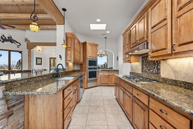 kitchen featuring stainless steel appliances, under cabinet range hood, a sink, a skylight, and tasteful backsplash