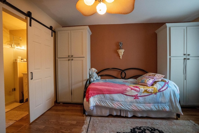 bedroom with ensuite bath, a ceiling fan, a barn door, and wood finished floors