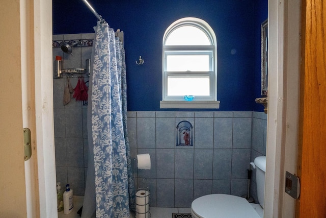 full bathroom featuring curtained shower, toilet, tile walls, and a wainscoted wall