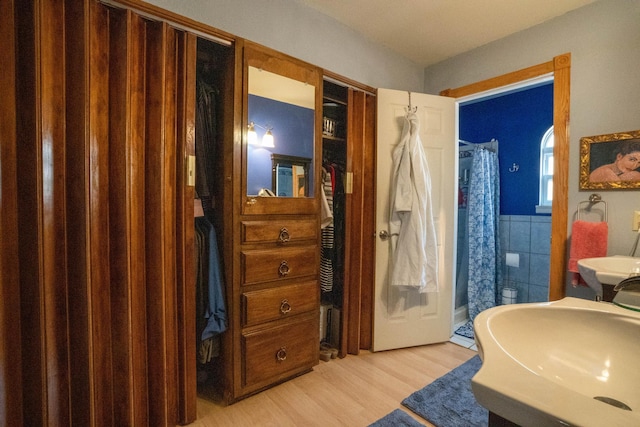 full bath featuring a shower with curtain, wood finished floors, a wainscoted wall, a sink, and tile walls