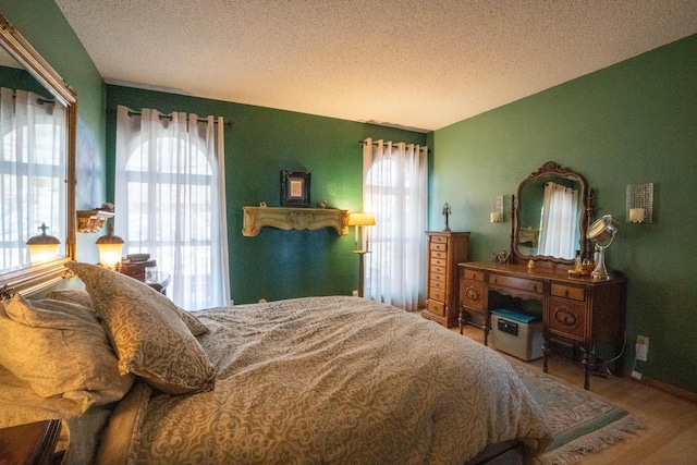 bedroom with multiple windows, a textured ceiling, baseboards, and wood finished floors