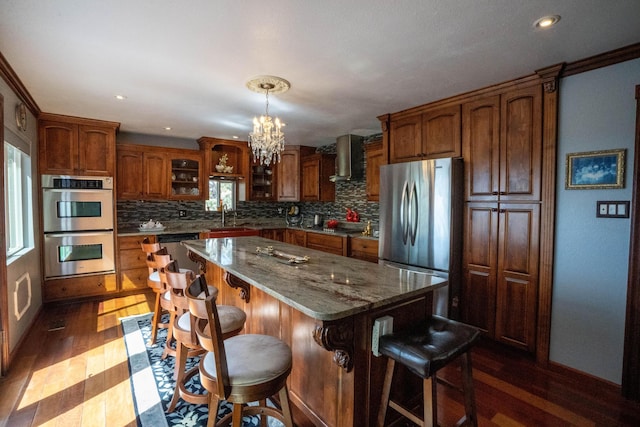 kitchen with a sink, a center island, wall chimney range hood, stainless steel appliances, and dark wood-style flooring