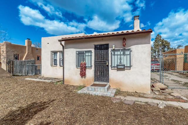 rear view of property featuring a gate, stucco siding, a chimney, and fence