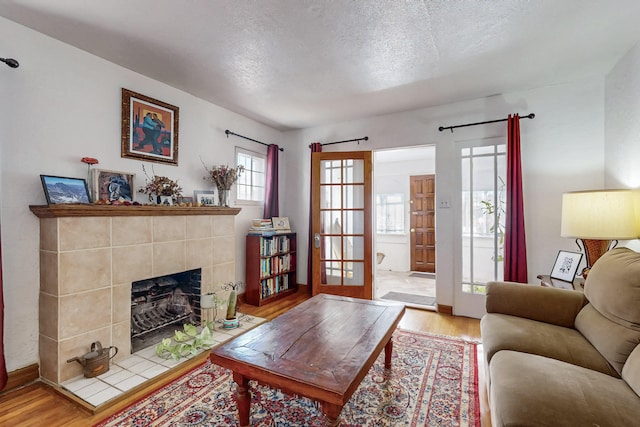 living room with a tile fireplace, a textured ceiling, and wood finished floors