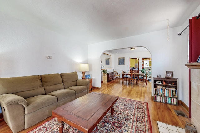 living area with light wood-style floors, visible vents, arched walkways, and baseboards