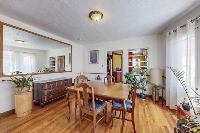 dining room featuring baseboards, light wood-type flooring, and a textured ceiling