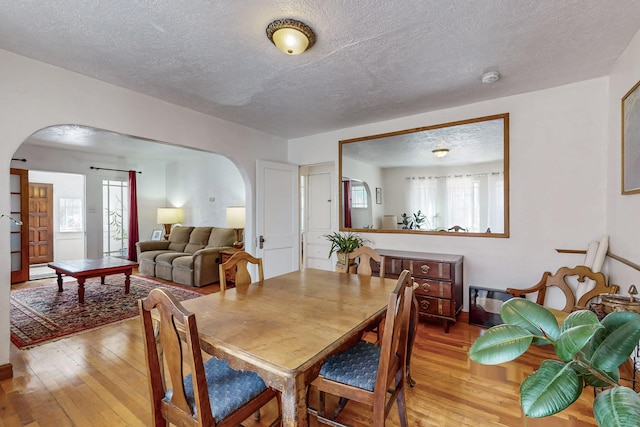 dining room with arched walkways, a textured ceiling, and light wood-type flooring