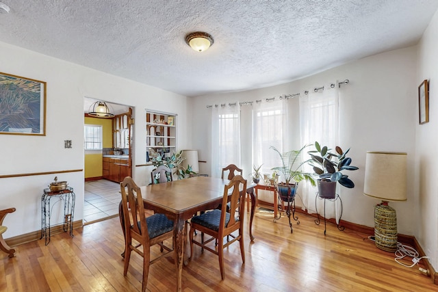 dining area featuring baseboards, light wood-type flooring, and a textured ceiling