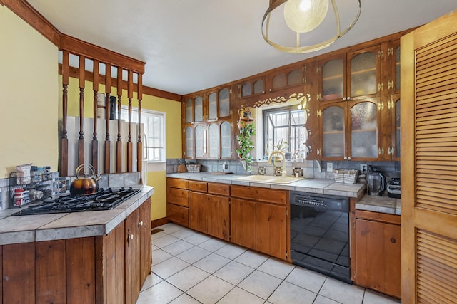 kitchen featuring glass insert cabinets, light tile patterned floors, decorative backsplash, black appliances, and a sink