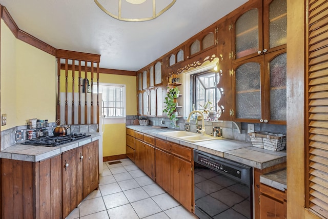 kitchen featuring glass insert cabinets, tile countertops, light tile patterned flooring, black appliances, and a sink