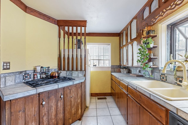 kitchen with tasteful backsplash, black gas cooktop, light countertops, light tile patterned flooring, and a sink