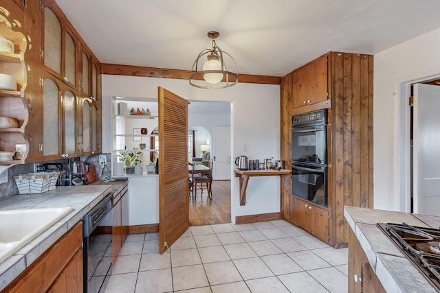 kitchen with light tile patterned floors, brown cabinets, black appliances, and tile countertops