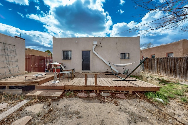 rear view of property featuring stucco siding, fence, and a wooden deck