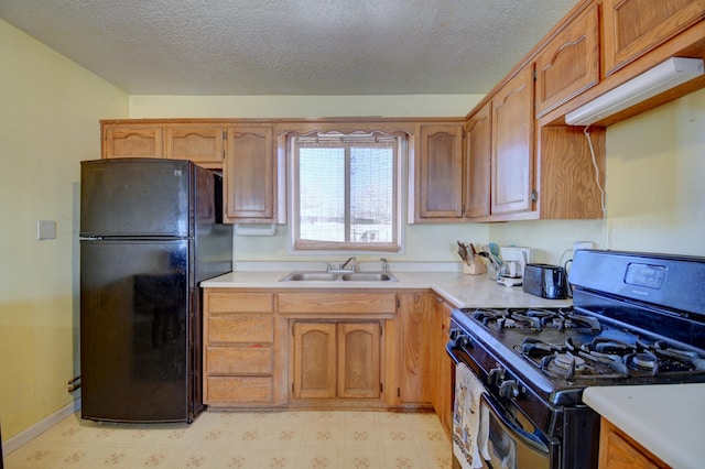 kitchen featuring a sink, gas range oven, freestanding refrigerator, light countertops, and light floors