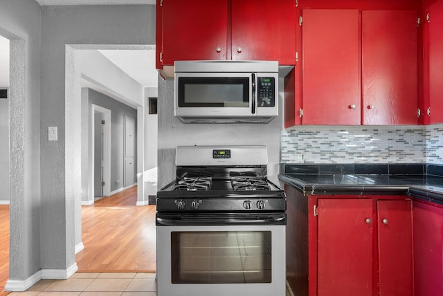 kitchen featuring red cabinetry, decorative backsplash, dark countertops, and appliances with stainless steel finishes