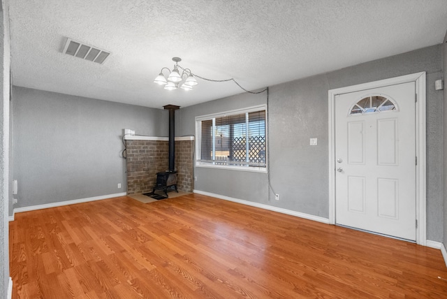 foyer featuring visible vents, a chandelier, a wood stove, wood finished floors, and a textured ceiling