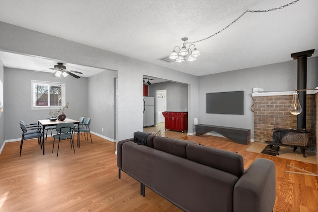 living room featuring ceiling fan with notable chandelier, a textured ceiling, light wood-type flooring, and a wood stove