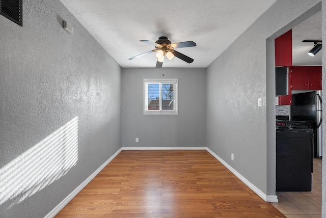 spare room featuring baseboards, ceiling fan, light wood-type flooring, a textured wall, and a textured ceiling