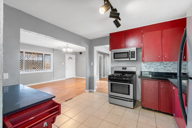 kitchen with tasteful backsplash, dark countertops, light tile patterned floors, red cabinets, and stainless steel appliances