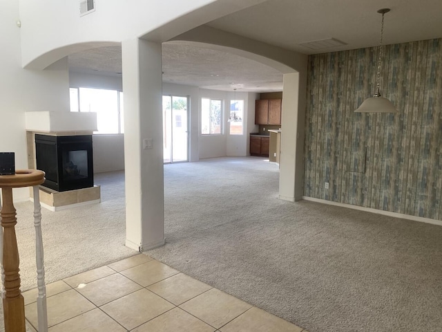unfurnished living room featuring visible vents, a multi sided fireplace, wood walls, light carpet, and arched walkways