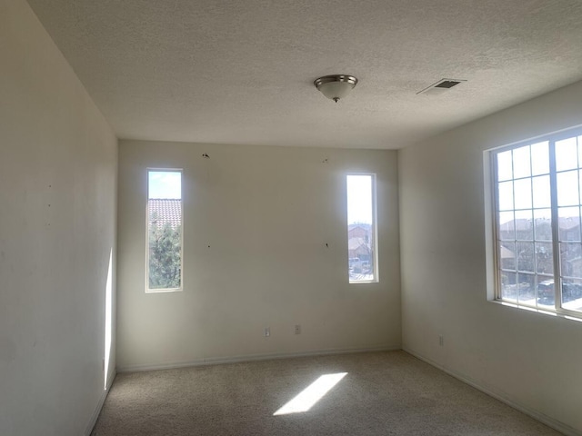 spare room with light carpet, visible vents, a textured ceiling, and baseboards