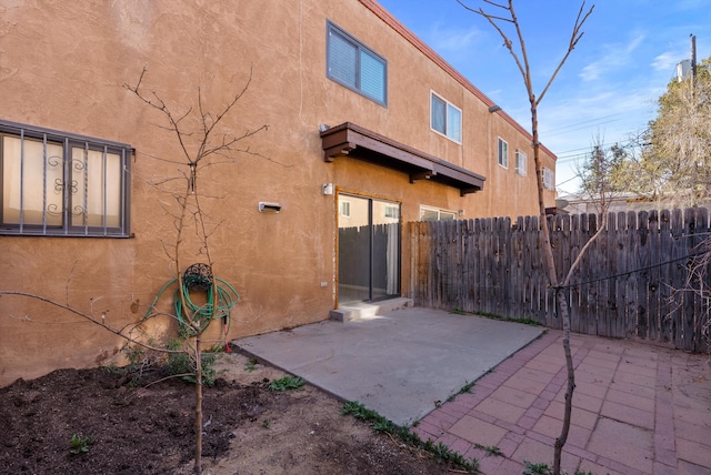 rear view of property featuring a patio area, fence, and stucco siding