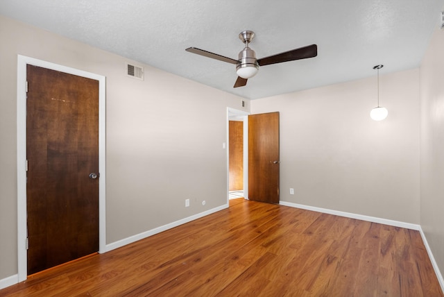 unfurnished bedroom with a ceiling fan, wood finished floors, visible vents, baseboards, and a textured ceiling