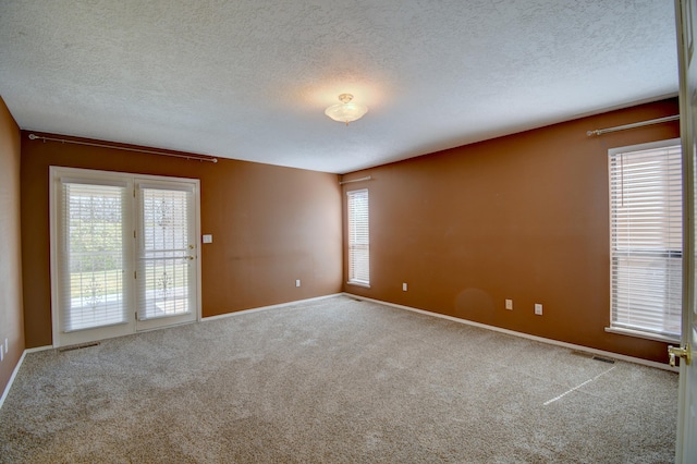 carpeted spare room featuring visible vents, a healthy amount of sunlight, a textured ceiling, and baseboards