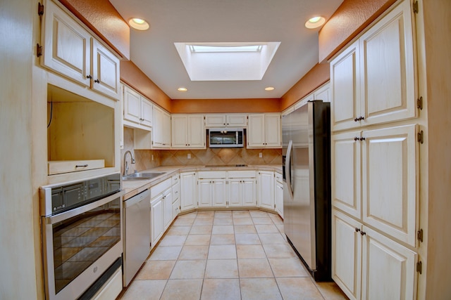 kitchen featuring backsplash, light countertops, appliances with stainless steel finishes, a skylight, and a sink