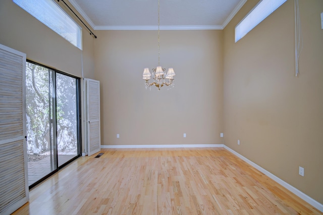 spare room featuring a chandelier, a healthy amount of sunlight, light wood finished floors, and ornamental molding