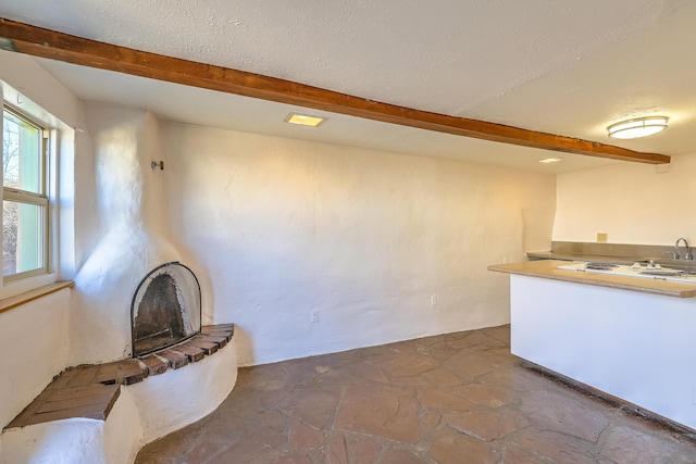 506 Onate Pl, Santa Fe, NM 87501 - unfurnished living room with a sink, stone tile floors, beamed ceiling, and a textured ceiling