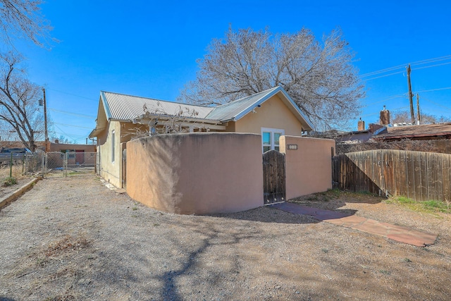 view of side of home with stucco siding, a gate, fence, and metal roof